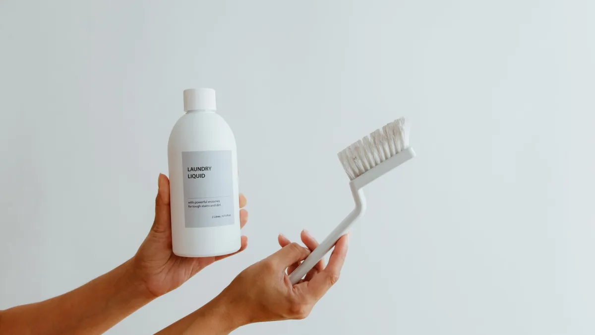 Borrifador com solução de vinagre branco e água ao lado de uma escova de cerdas macias.