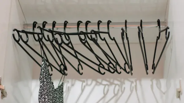 Cabide com várias peças de roupa preta penduradas em um closet.