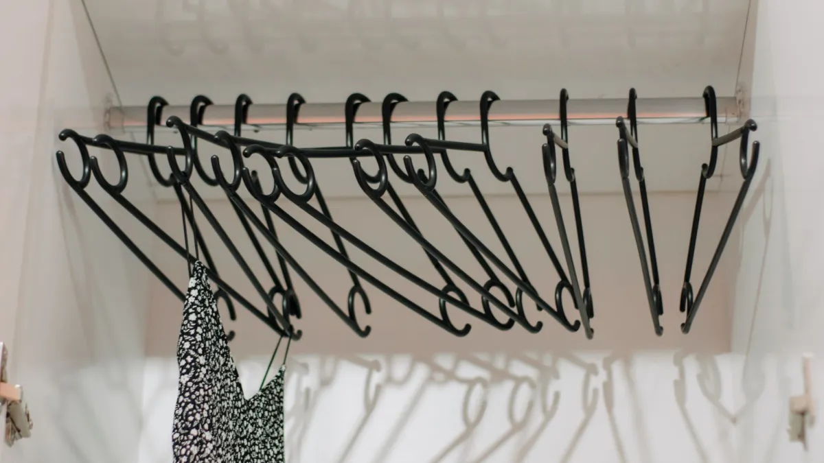 Cabide com várias peças de roupa preta penduradas em um closet.