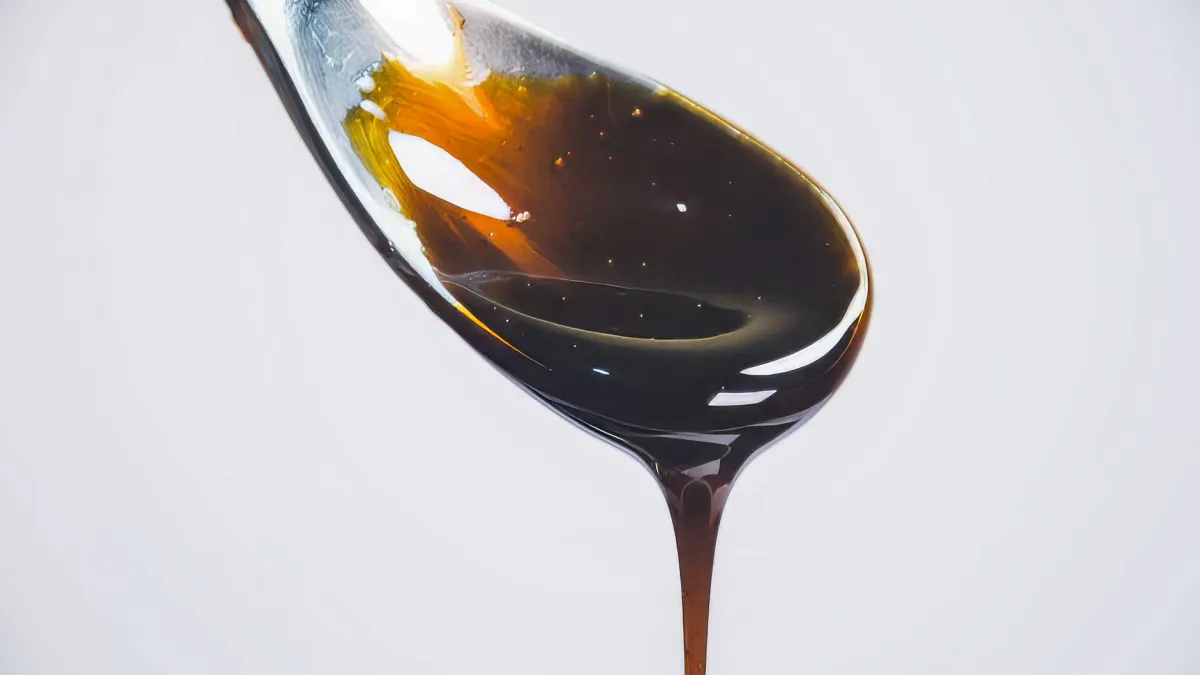 Calda de caramelo quente escorrendo de uma colher, com um ambiente de cozinha que sugere alta temperatura.