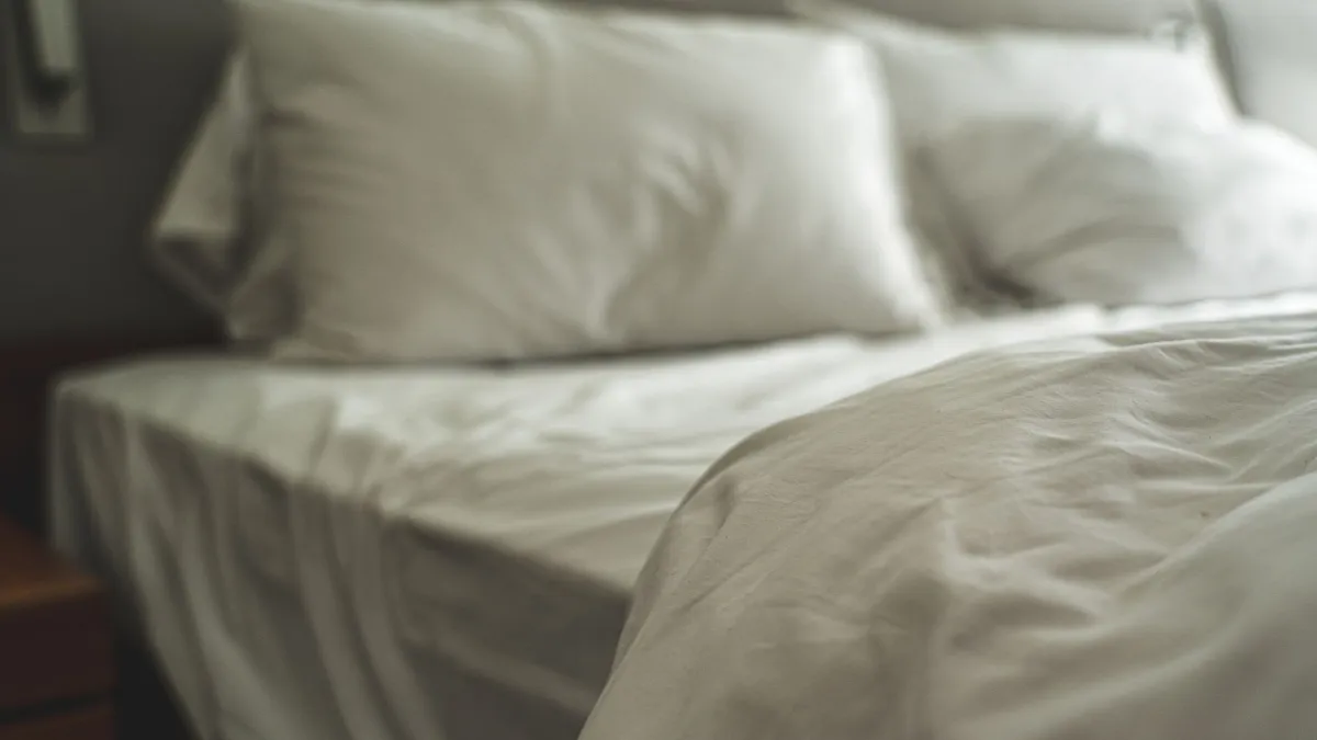 Cama com lençóis de algodão em tons claros, promovendo conforto térmico.