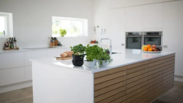 Cozinha clara e arejada com uma janela aberta e vasos de ervas frescas na bancada.
