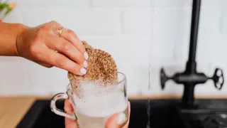 Esponja de cozinha sendo lavada em água corrente para remover gordura
