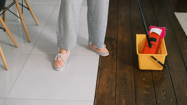 Mão usando esfregão em um piso limpo e brilhante, com balde ao lado.