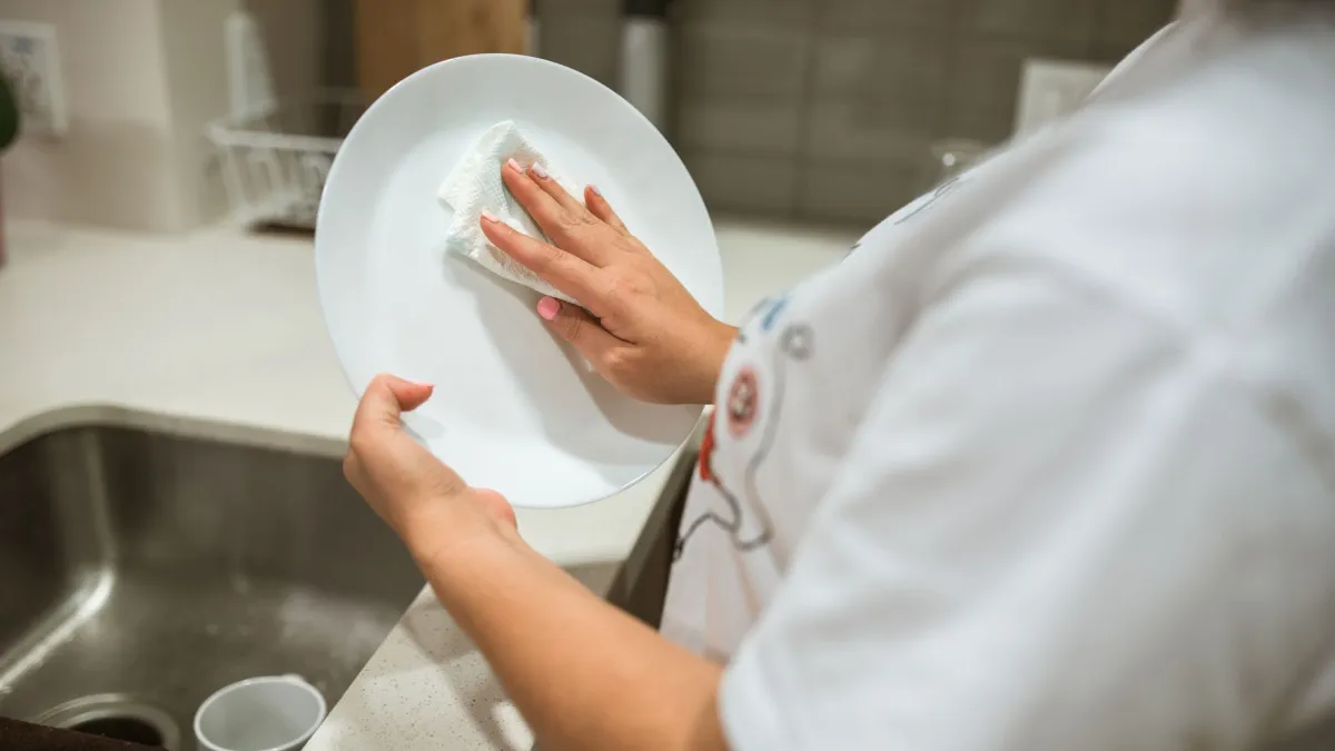 Mãos lavando panos de prato brancos em uma pia com espuma.