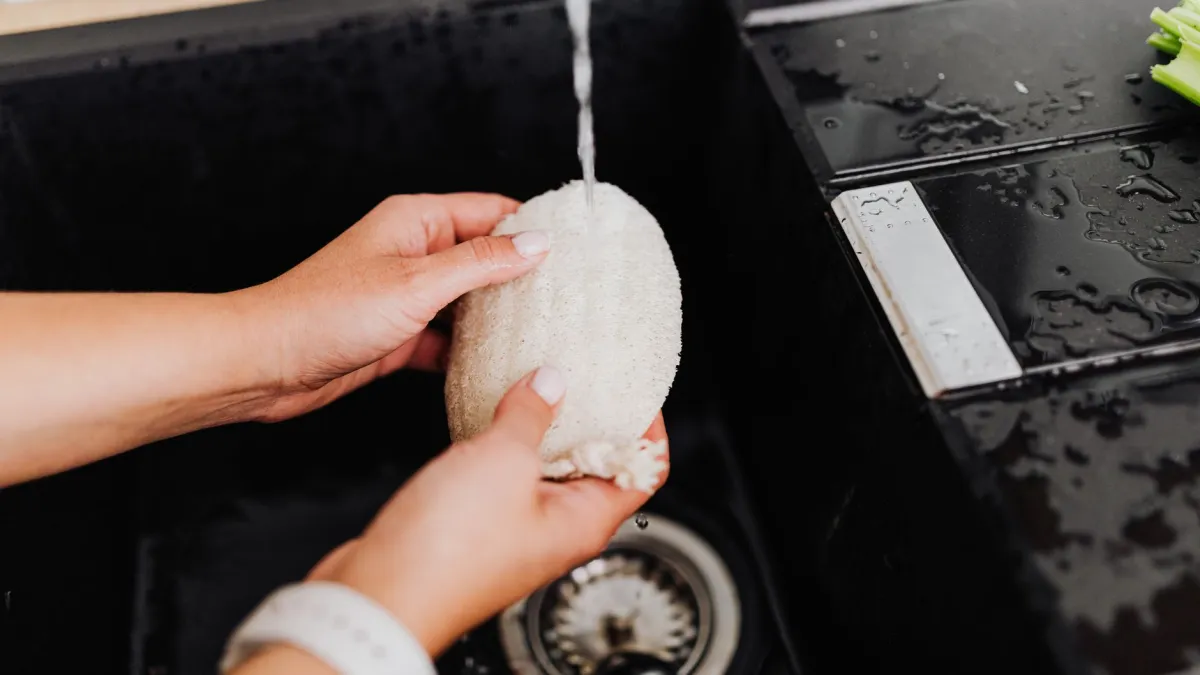 Mulher lavando um recipiente plástico na pia da cozinha