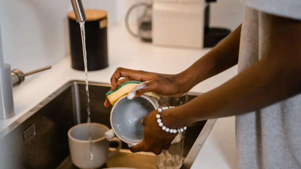 Mulher limpando a pia da cozinha com esponja e espuma de sabão.