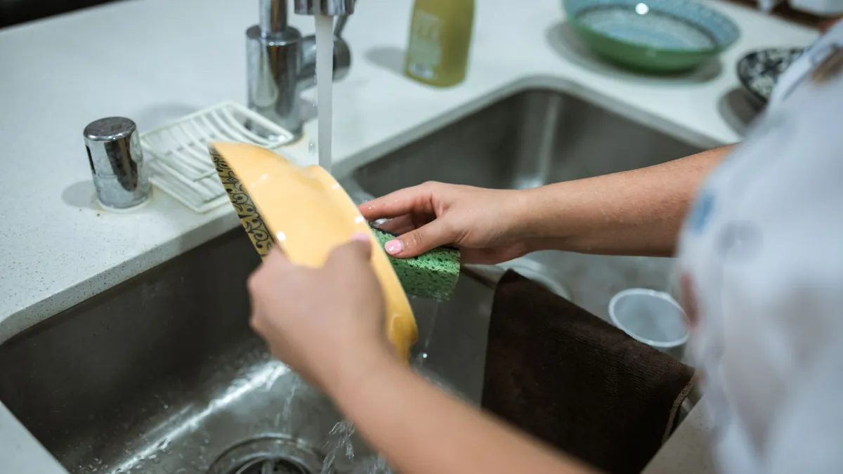 Mulher limpando a pia da cozinha com uma esponja e detergente.