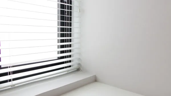 Mulher limpando persianas brancas com um pano macio em um quarto iluminado