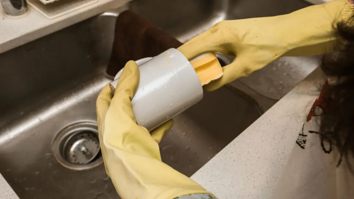 Mulher limpando rodapé de cozinha com uma esponja e solução de limpeza
