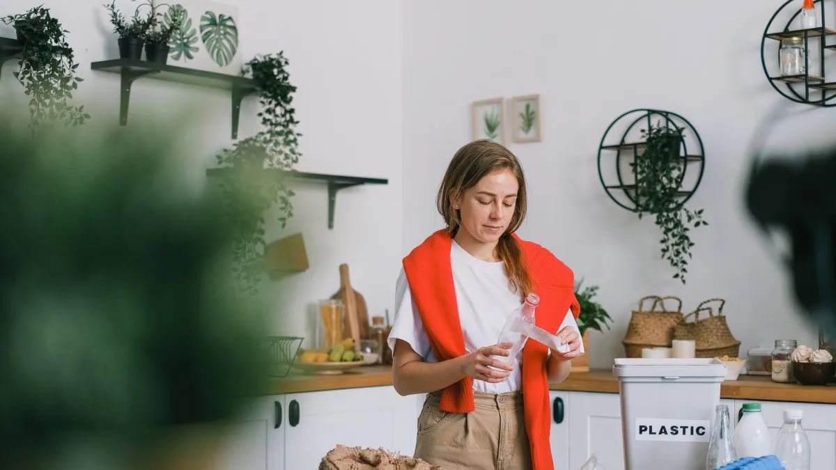 Mulher separando recicláveis de lixo orgânico na cozinha.