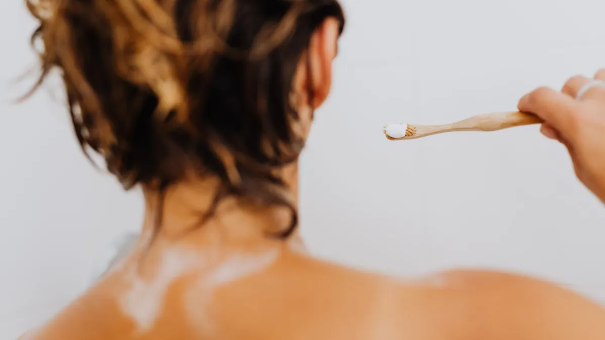 Pessoa limpando o ralo do chuveiro com uma escova para remover cabelos e resíduos.