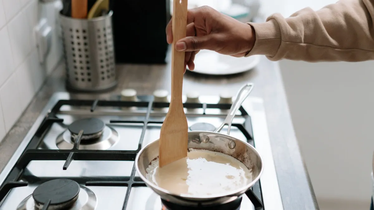 Pessoa raspando resíduos queimados de uma panela de inox com espátula