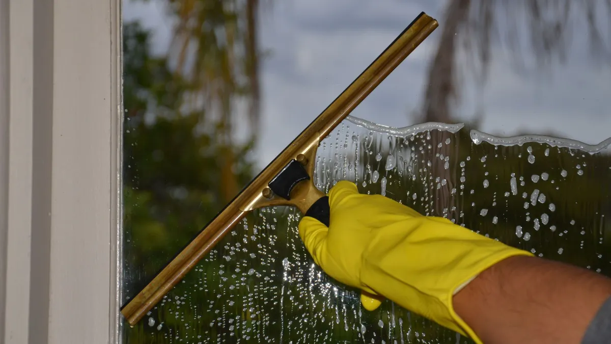Rodo para vidros sendo usado para secar um vidro de janela limpo, sem deixar manchas.