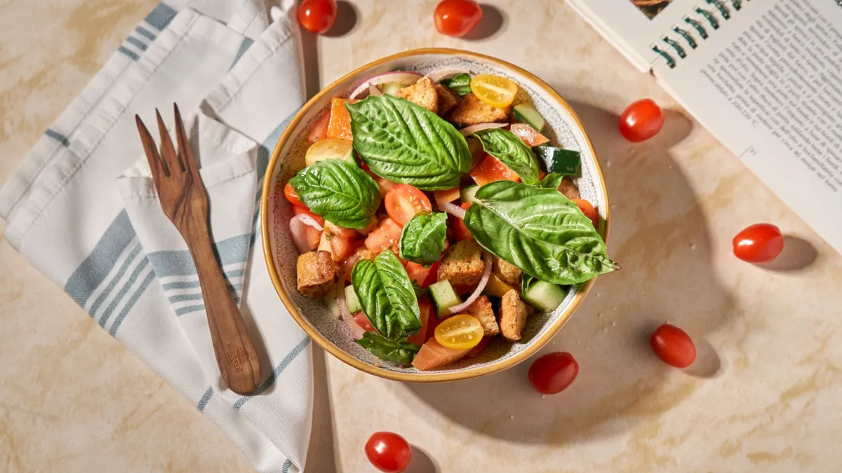 Salada panzanella colorida em uma travessa rústica, com pedaços de pão, tomates e manjericão.