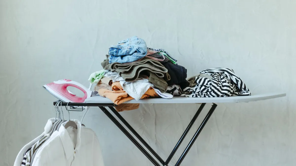 Tábua de passar roupa com roupas limpas e passadas, com um ferro de passar ao lado.