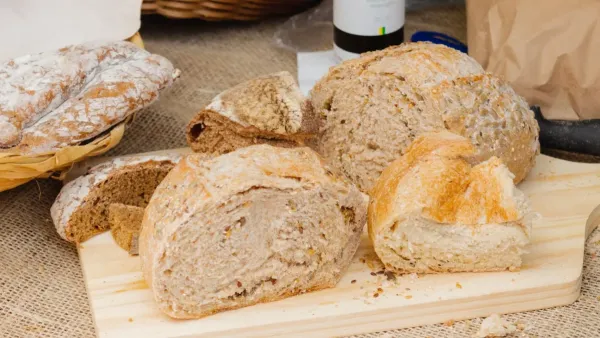 Um pão amanhecido sobre uma mesa de madeira rústica, com alguns farelos espalhados.