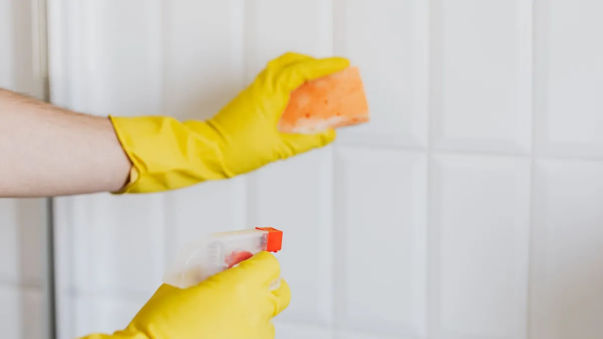 Uma mão com luva limpando manchas de mofo de rejuntes de azulejos com um pano e spray.